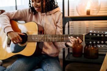 Woman sitting on the floor and play the guitar at home, closeup view. Pretty lady with musical instrument relax in the room, female music lover resting