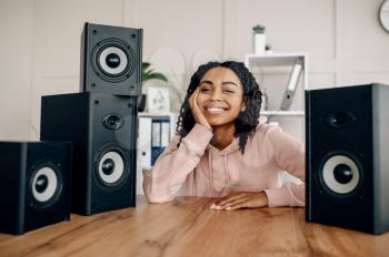 Cute happy woman between many audio speakers and listen to music. Pretty lady relax in the room, female sound lover resting