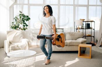 Attractive woman with guitar poses at home. Pretty lady with musical instrument relax in the room, female music lover resting