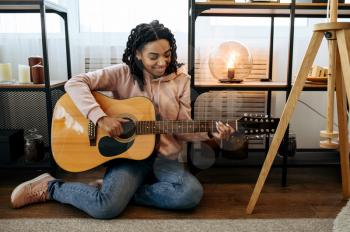 Woman sitting on the floor and play the guitar at home, closeup view. Pretty lady with musical instrument relax in the room, female music lover resting