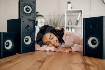 Cute happy woman between many audio speakers and listen to music. Pretty lady relax in the room, female sound lover resting