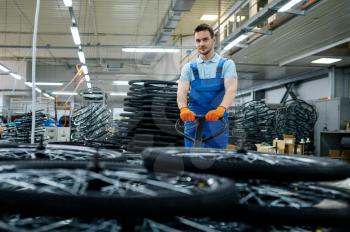 Male worker carries bicycle wheels on a cart on factory. Bike rims assembly line in workshop, cycle parts installation, modern technology