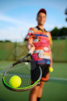 Young male tennis player poses with racket and ball on outdoor court. Active healthy lifestyle, sport game competition, fitness training with racquet