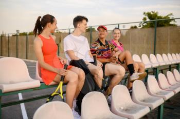 Mixed doubles tennis players are resting on the podium, outdoor court. Active healthy lifestyle, sport game training, fitness workout with racquets