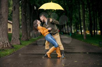 Happy love couple dancing in park in summer rainy day. Man and woman hugs under umbrella in rain, romantic date on walking path, wet weather in alley