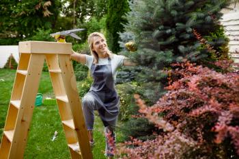 Attractive woman with pruners climbs the stairs in the garden. Female gardener takes care of plants outdoor, gardening hobby, florist lifestyle and leisure