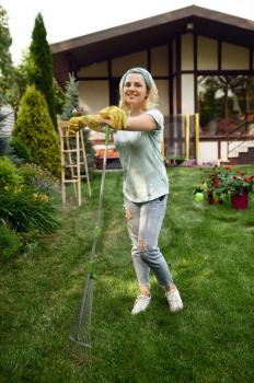 Smiling woman with rake works in the garden. Female gardener takes care of plants outdoor, gardening hobby, florist lifestyle