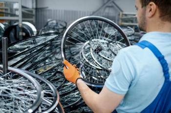 Mechanic in uniform holds bicycle wheel on factory. Bike rims and spokes assembly in workshop, cycle parts installation