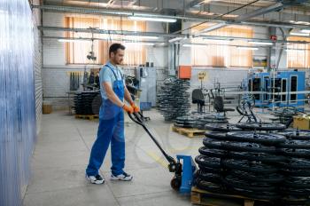 Male worker carries bicycle wheels on a cart on factory. Bike rims assembly line in workshop, cycle parts installation, modern technology