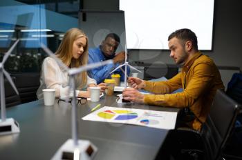 Team of young managers with wind mill models, conference in IT office. Professional teamwork and planning, group brainstorming and corporate work, meeting of colleagues