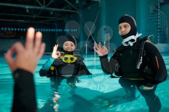 Instructor and two divers in suits, course in diving school. Teaching people to swim underwater with scuba gear, indoor swimming pool interior on background, group training