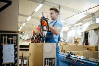 Bicycle factory, worker packs teen bike in box. Male mechanic in uniform installs cycle parts, assembly line in workshop, industrial manufacturing