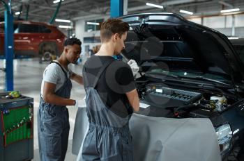 Two male workers repairs engine, car service. Vehicle repairing garage, men in uniform, automobile station interior on background. Professional auto diagnostic