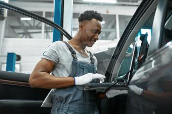 Male mechanic using laptop at the auto with opened hood, car service. Vehicle repairing garage, man in uniform, automobile station interior