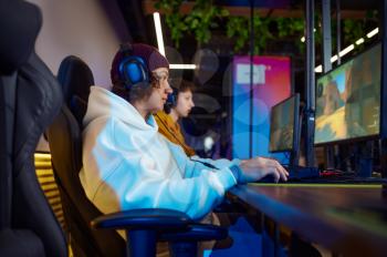 Two young gamers in headsets play in video game club. Virtual entertainment, e-sport tournament, cybersport lifestyle. Male person leisures in internet cafe