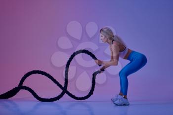 Young sportswoman with ropes poses in studio, neon background, crossfit. Fitness woman at the photo shoot, sport concept, active lifestyle motivation