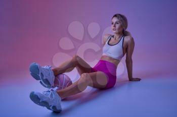 Young sexy sportswoman with ball sitting on the floor in studio, neon background. Fitness woman at the photo shoot, sport concept, active lifestyle