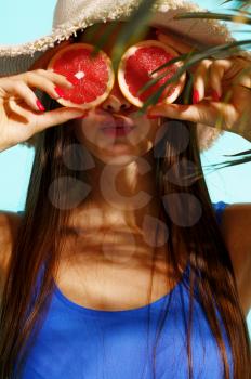Pretty woman in swimsuit poses with fruits in studio, cyan background. Girl in swimwear ready to take a tan. Model with slim body in swimming underwear, seductive female swimmer