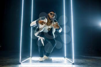 Stylish rapper in gold jewelry and sunglasses, dark background. Hip-hop performer, rap singer, break-dance performing, entertainment lifestyle