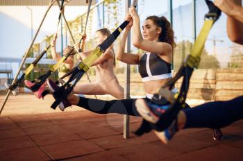 Women's group doing exercise with ropes on sports ground, outdoors fitness training. Slim female athletes in sportswear, team fit workout, teamwork