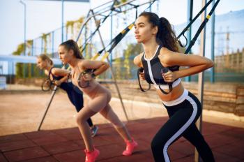 Slim women doing fit exercise with ropes on sports ground, outdoors group training. Female athletes in sportswear, team fitness workout, teamwork