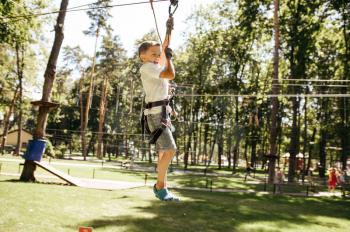 Little brave boy on zipline in rope park, playground. Child climbing on suspension bridge, extreme sport adventure on vacations, danger entertainment outdoors
