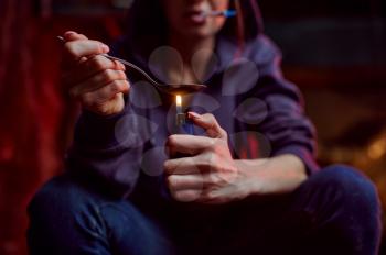 Drug addict woman with spoon and fire prepares dose, shebang interior on background, den. Narcotic addiction problem, eternal depression
