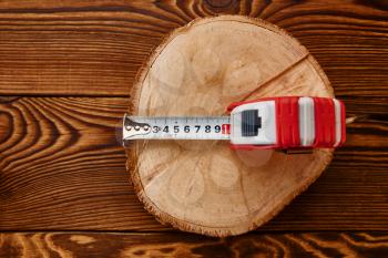 Measuring tape on stump, wooden background, top view, nobody. Professional instrument, carpenter equipment, woodworker tools