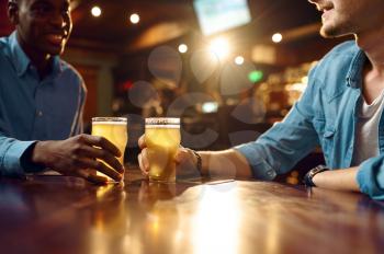 Two male friends drinks fresh beer in bar. People relax in pub, night lifestyle, friendship, event celebration, men leisures in restaurant