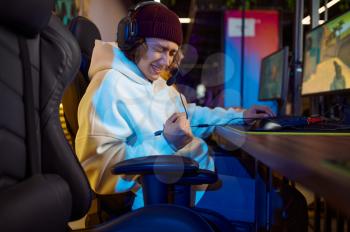 Young gamer in headphones play in game club. Virtual entertainment, e-sport tournament, cybersport lifestyle. Male person leisures in internet cafe