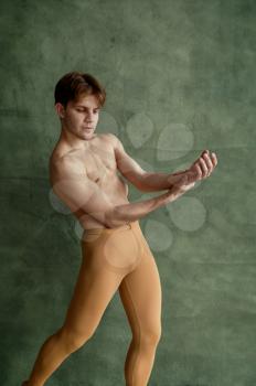 Male ballet dancer, training in dancing class, grunge wall on background. Performer with muscular body, elegance of movements