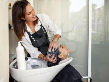 Hairdresser washes woman's hair, top view, hairdressing salon. Stylist and client in hairsalon. Beauty business, professional service