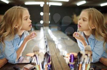 Little girl using lipstick at the mirror in makeup salon. Mom and daughter play stylists together, happy childhood, glamour family, make-up artist