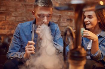 Young love couple relax in hookah bar, hooka smoke. Shisha smoking, traditional bong culture, tobacco aroma for relaxation, rest with hooka