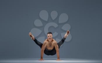 Male yoga doing stretching exercise in studio, grey background. Strong man practicing yogi , asana training, top concentration, healthy lifestyle