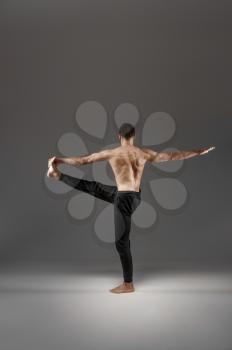 Muscular male yoga doing stretching exercise in studio, grey background. Strong man practicing yogi , asana training, top concentration, healthy lifestyle