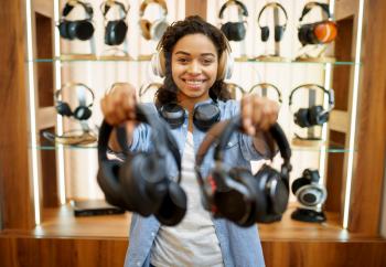 Woman shows headphones in audio components store, music lover. Female person in music shop, showcase with earphones on background, buyer in multimedia salon