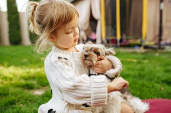 Kid embracing funny dog in the garden, best friends. Child with puppy sitting on the lawn on backyard. Little girl and her pet having fun on playground outdoors, happy childhood