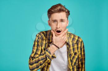 Young surprised man portrait, blue background, emotion. Face expression, male person looking on camera in studio, emotional concept, positive feelings