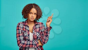 Young woman points up, blue background, positive emotion. Face expression, female person looking on camera in studio, emotional concept, feelings