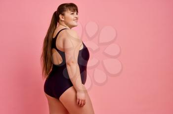 Overweight woman poses in swimsuit, body positive, pink background. Obesity fighting, cheerful female person without complexes, striving for a healthy lifestyle