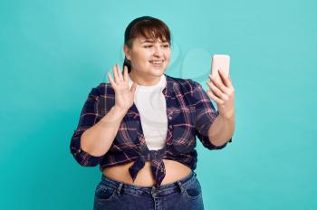 Funny overweight woman makes selfie, body positive, blue background. Obesity fighting, cheerful female person without complexes