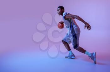 Basketball player practicing with ball in studio, neon background. Professional male baller in sportswear playing sport game, tall sportsman