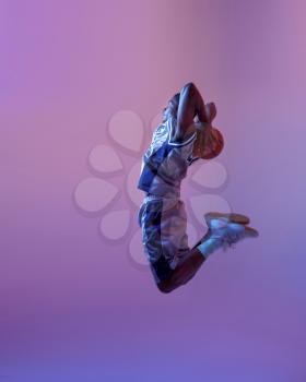 Basketball player jumping with ball in studio, neon background. Professional male baller in sportswear playing sport game