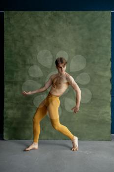 Male ballet dancer, training in dancing class, grunge wall on background. Performer with muscular body, elegance of movements