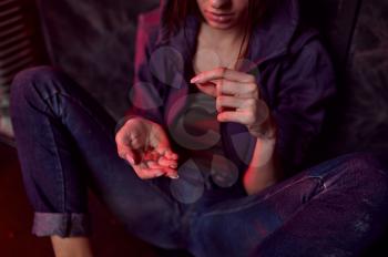 Drug addict female person holds pills, shebang interior on background, den. Narcotic addiction problem, eternal depression of junky people