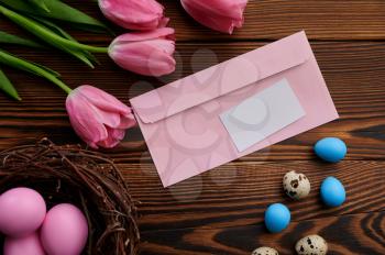 Pink tulips, easter eggs and greeting envelope on wooden background. Spring flowers blooming and paschal food, fresh floral decoration, holiday celebration symbol