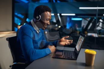 One man in headphones works on laptop in night office. Male worker, dark business center interior on background, modern workplace