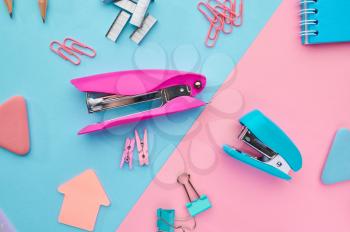 Stapler and paper clips closeup, blue and pink background. Office stationery supplies, school or education accessories
