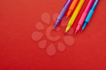 Colorful pens with caps closeup, red background. Office stationery supplies, school or education accessories, writing and drawing tools